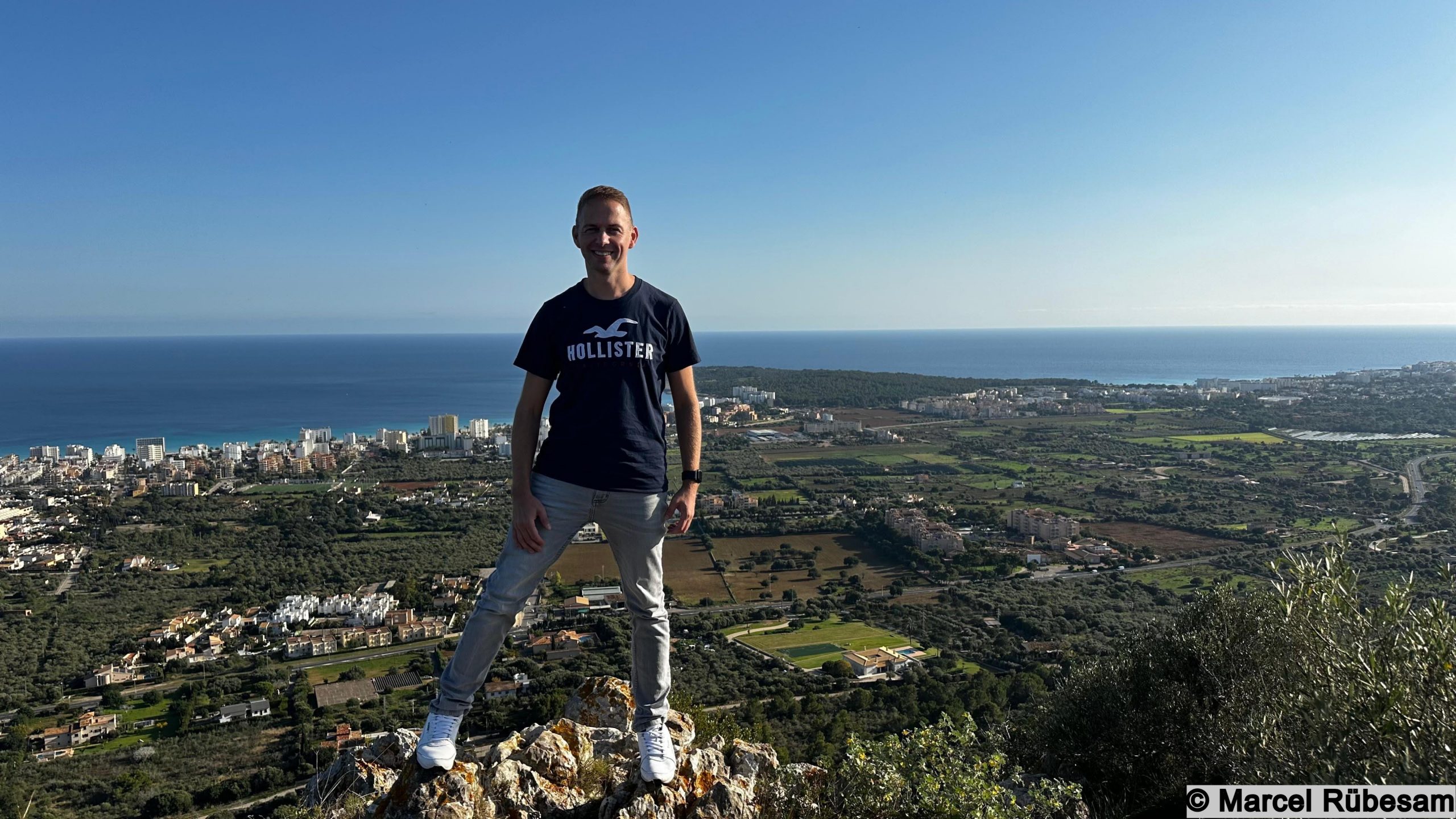Marcel Rübesam steht auf dem Gipfel des Puig de na Penyal auf Mallorca mit Blick auf die Küste und Cala Millor im Hintergrund