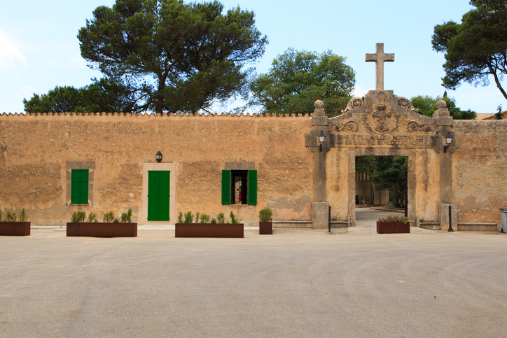 Frontansicht des Santuari de Cura mit Kreuz, Inschrift und grünen Fensterläden auf Mallorca.