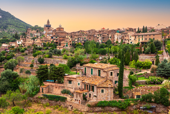 Traditionelle Häuser in Valldemossa vor der Kulisse der Tramuntana-Berge auf Mallorca bei Sonnenuntergang.