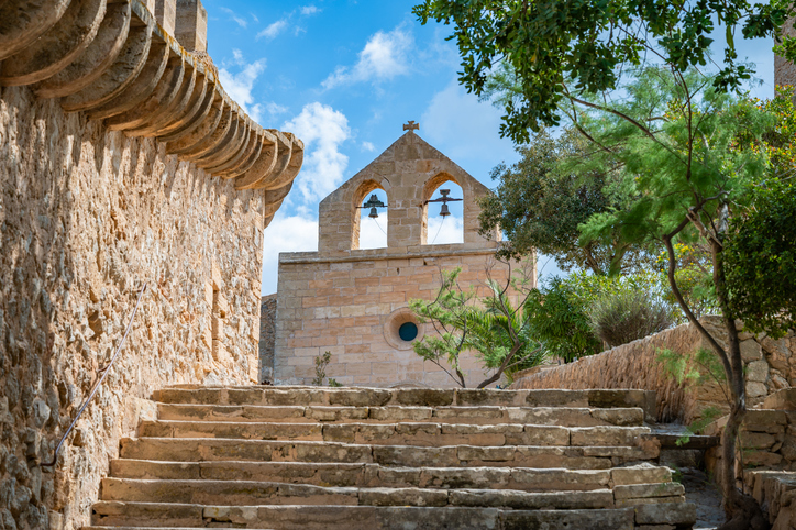 Steintreppe führt hinauf zur Kirche mit Glocken am Castell de Capdepera auf Mallorca bei blauem Himmel.