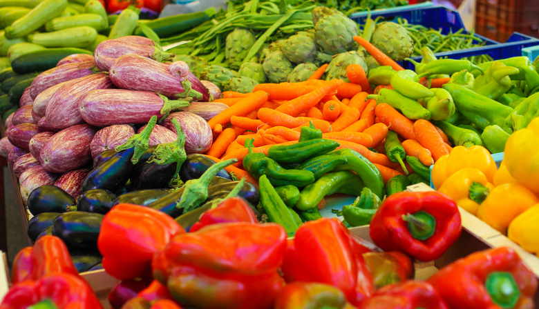Bunte Auswahl an frischem Gemüse auf einem mallorquinischen Marktstand, darunter Paprika, Auberginen, Möhren und Artischocken.