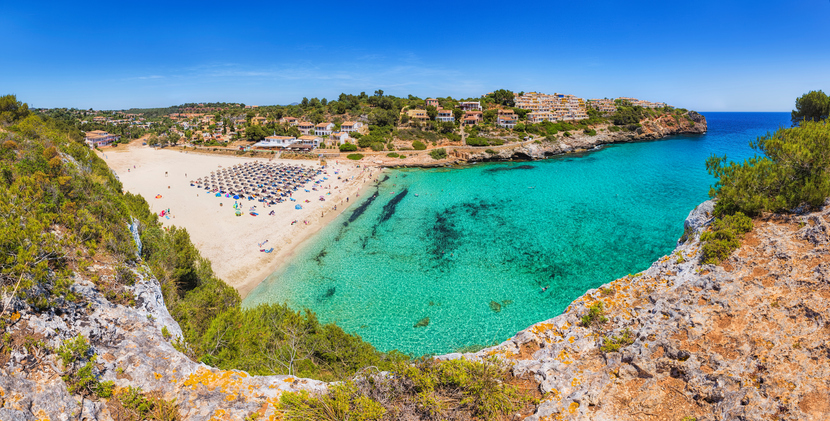 Panoramaaufnahme der Bucht Cala Romàntica mit kristallklarem Wasser, Sandstrand und umliegenden Ferienhäusern auf Mallorca.