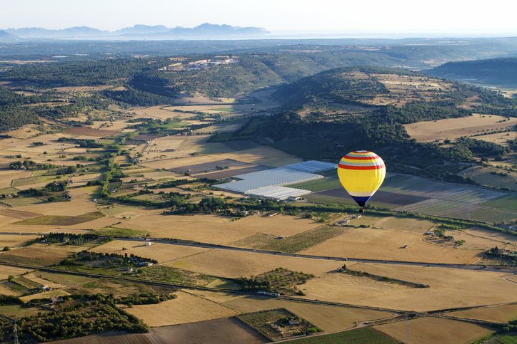Heißluftballon schwebt über Felder und Hügel auf Mallorca mit weitem Blick bis zum Horizont.