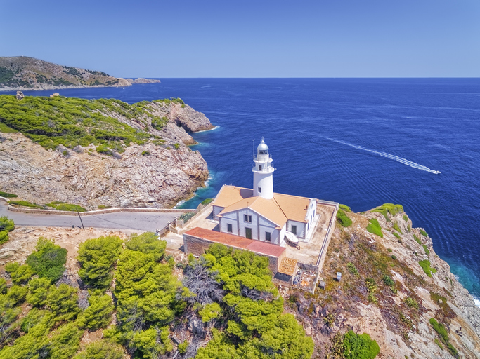 Weißer Leuchtturm Far de Capdepera auf einer Klippe über dem Meer bei Capdepera auf Mallorca, umgeben von Pinien und Felsen.