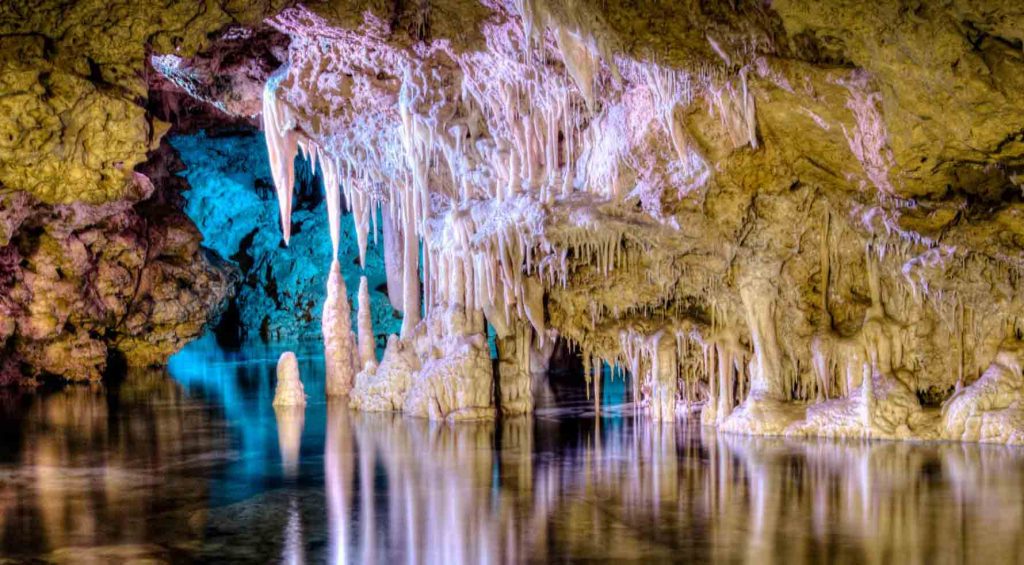 Stalaktiten und Stalagmiten spiegeln sich im klaren Wasser des unterirdischen Sees in den Cuevas dels Hams