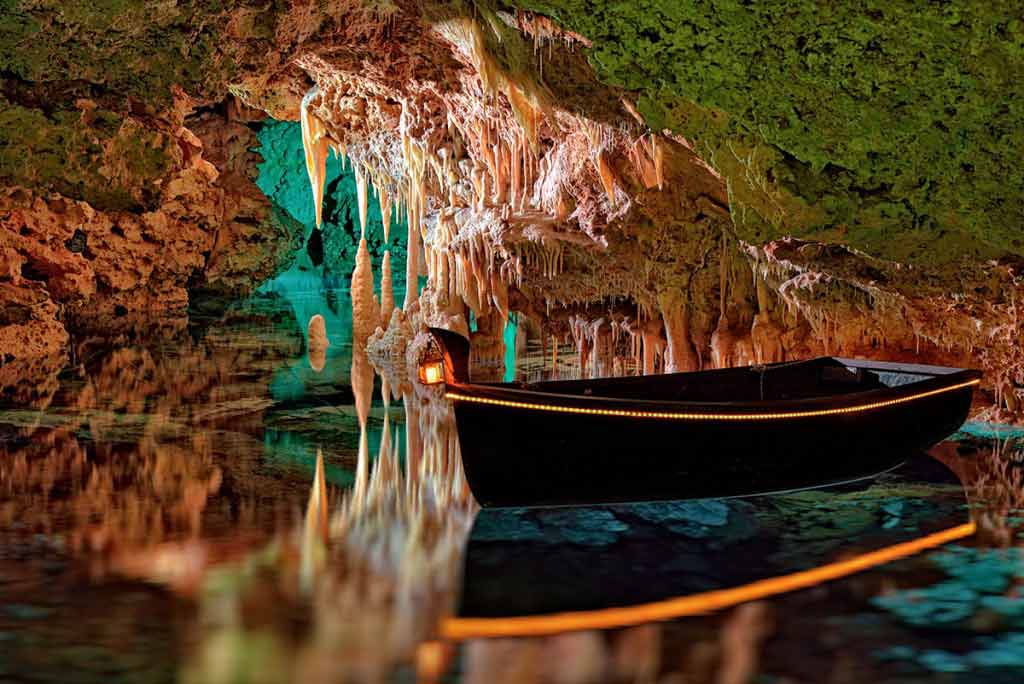 Beleuchtetes Boot auf einem unterirdischen See mit Tropfsteinen in den Hams-Höhlen auf Mallorca