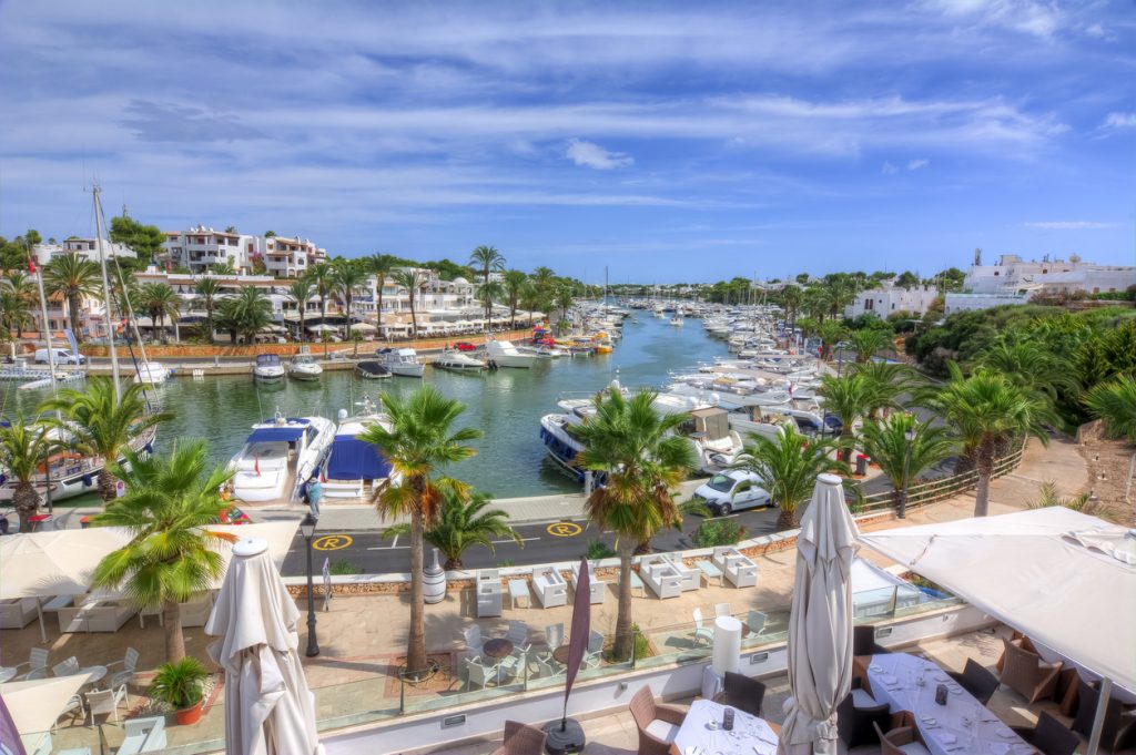 Blick auf den Yachthafen von Cala d’Or auf Mallorca mit zahlreichen Booten, Palmen und Restaurants an der Promenade.