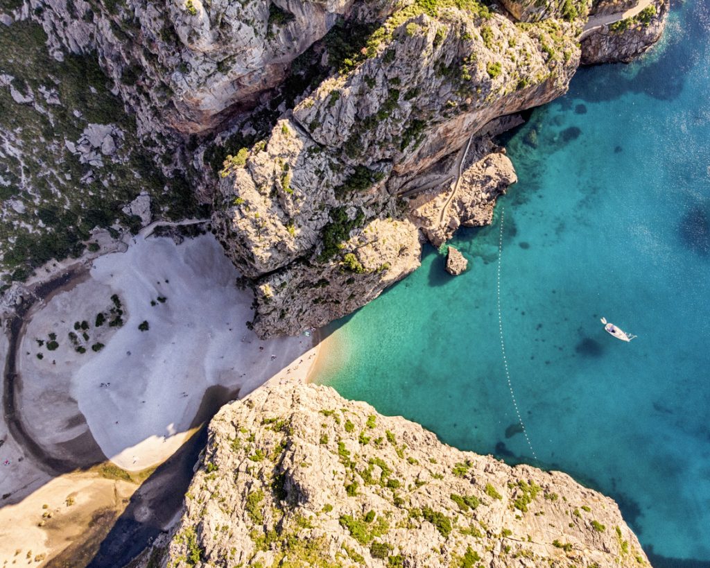 Luftaufnahme von Sa Calobra auf Mallorca mit türkisfarbenem Wasser, Sandstrand und imposanten Felsen.