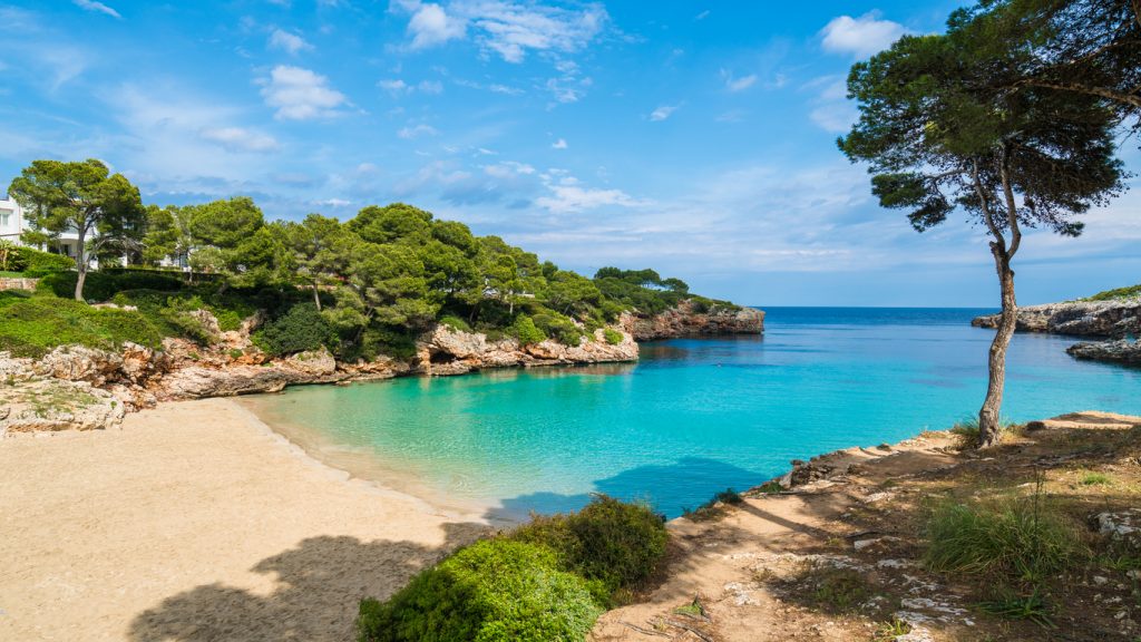 Ruhige Bucht in Cala d’Or mit klarem türkisfarbenem Wasser, Sandstrand und umgebender Natur