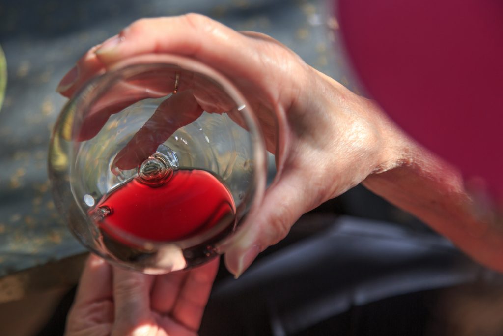 Nahaufnahme einer Hand, die ein Glas mit rotem Wein bei einer Weinprobe auf Mallorca hält.