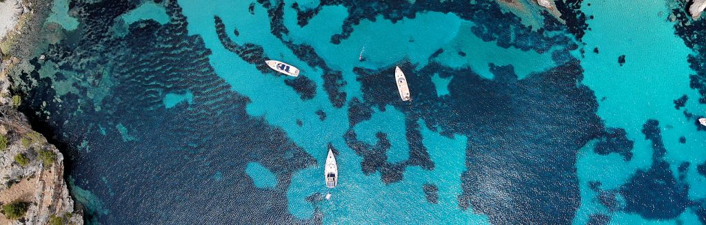 Drohnenaufnahme zeigt mehrere Yachten in der klaren, türkisfarbenen Bucht Cala Blanca vor der felsigen Küste Mallorcas