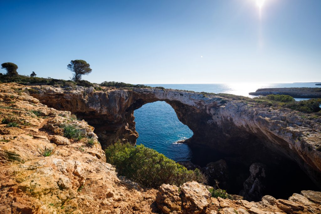 Natürlicher Felsbogen an der Küste der Cala Varques auf Mallorca mit Blick auf das tiefblaue Mittelmeer.