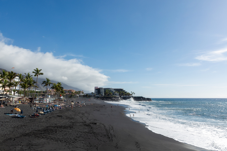 Menschen entspannen am dunklen Sandstrand Playa de Puerto Naos auf La Palma mit Palmen und Brandung