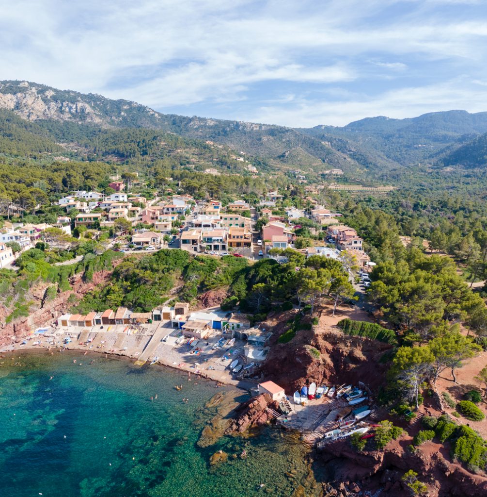 Drohnenaufnahme von Port des Canonge mit kleinen Bootshäusern, Kiesstrand und mediterraner Hügellandschaft