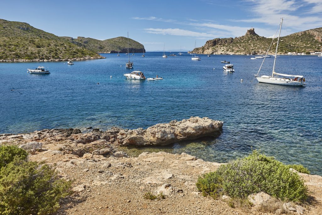 Mehrere Segel- und Motorboote ankern in der türkisblauen Bucht vor der felsigen Küste der Insel Cabrera