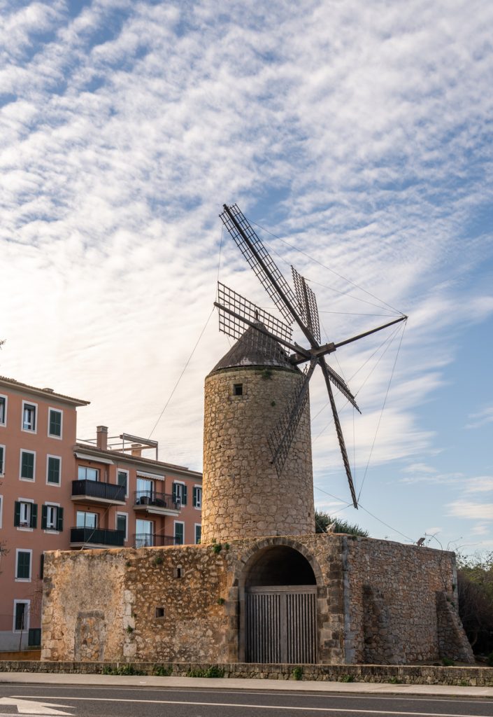 Traditionelle Stein-Windmühle bei Llucmajor auf Mallorca mit blauen Himmel und Gebäuden im Hintergrund.