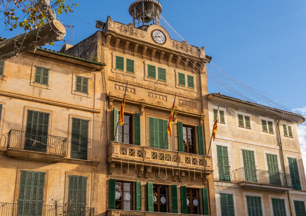 Fassade des historischen Rathauses von Llucmajor mit mallorquinischen Flaggen und grünen Fensterläden.