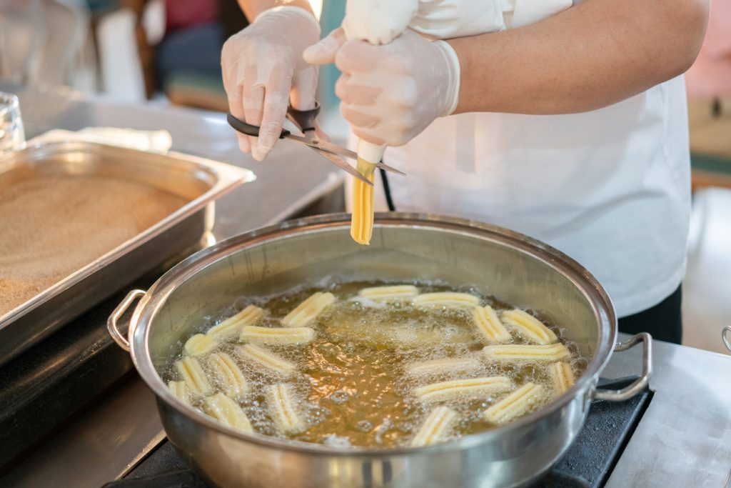Koch formt und frittiert Churros-Teig frisch in heißem Öl