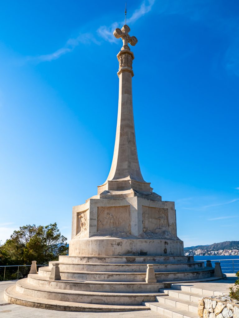 Großes Stein-Kreuzdenkmal auf einem runden Podest in Santa Ponsa auf Mallorca, mit blauen Himmel und Meer im Hintergrund.