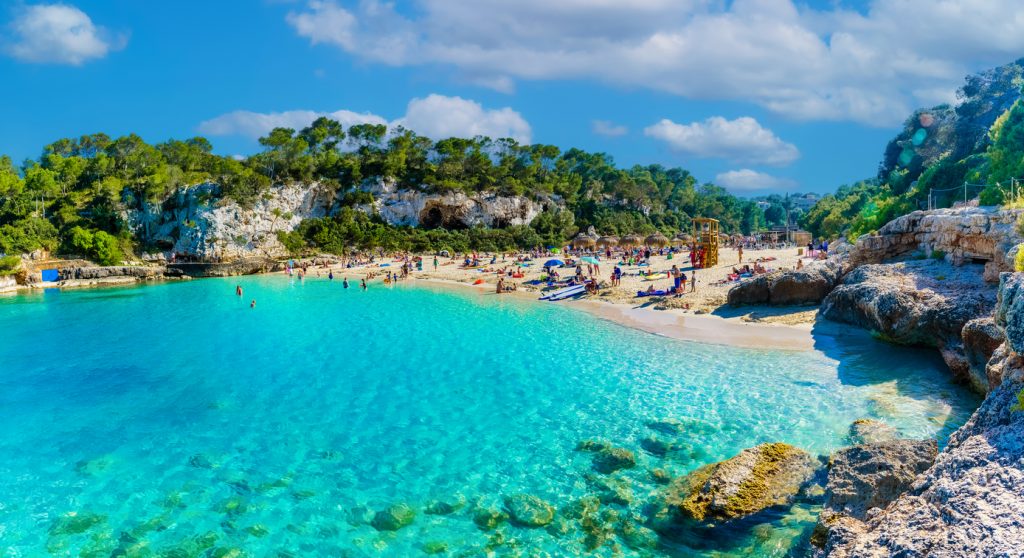 Cala Llombards auf Mallorca mit kristallklarem Wasser, weißem Sandstrand und grünen Felsen im Hintergrund.