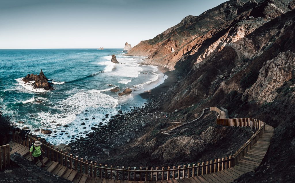 Playa de Benijo auf Teneriffa mit schwarzem Sandstrand, Felsen im Meer und Holztreppe entlang der Steilküste.