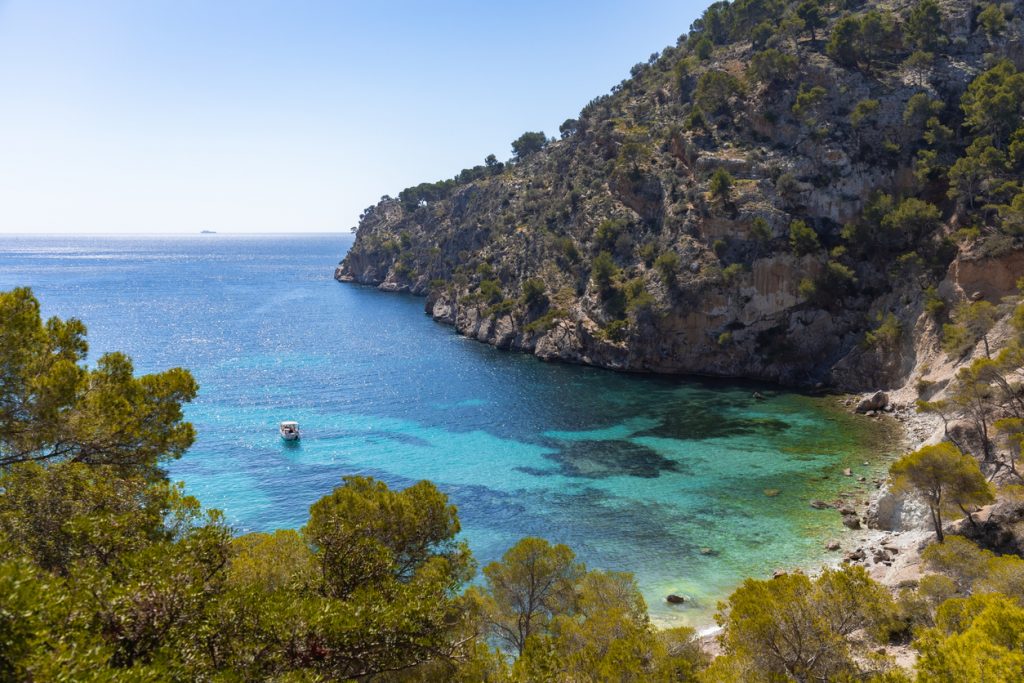 Panoramablick auf die felsige Bucht Cala Blanca mit türkisfarbenem Meer und einem Boot vor der Küste von Mallorca