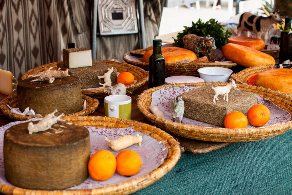 Rustikaler Marktstand mit großen Käselaiben, Zitrusfrüchten und Tierfiguren bei einem Frühlingsfest auf Mallorca