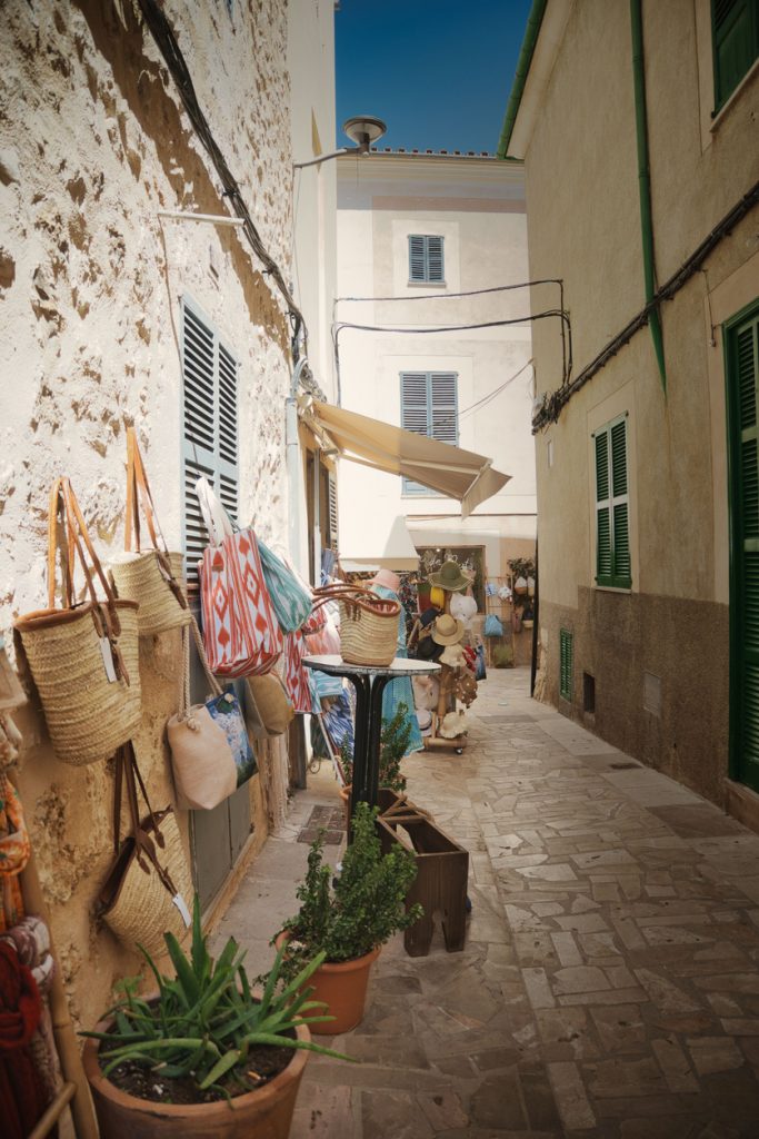Schmale Gasse in Sineu auf Mallorca mit kleinen Marktständen, Taschen, Pflanzen und traditionellen Produkten während eines Markttages.