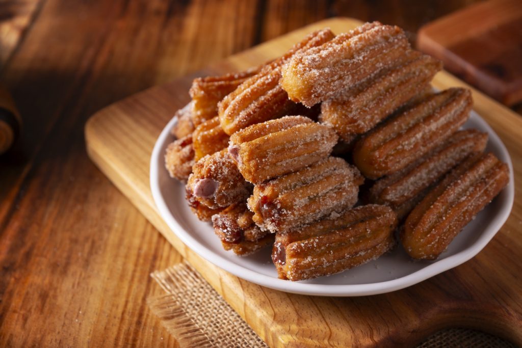Zuckerbestäubte, gefüllte Churros auf einem weißen Teller, serviert auf einem Holzbrett