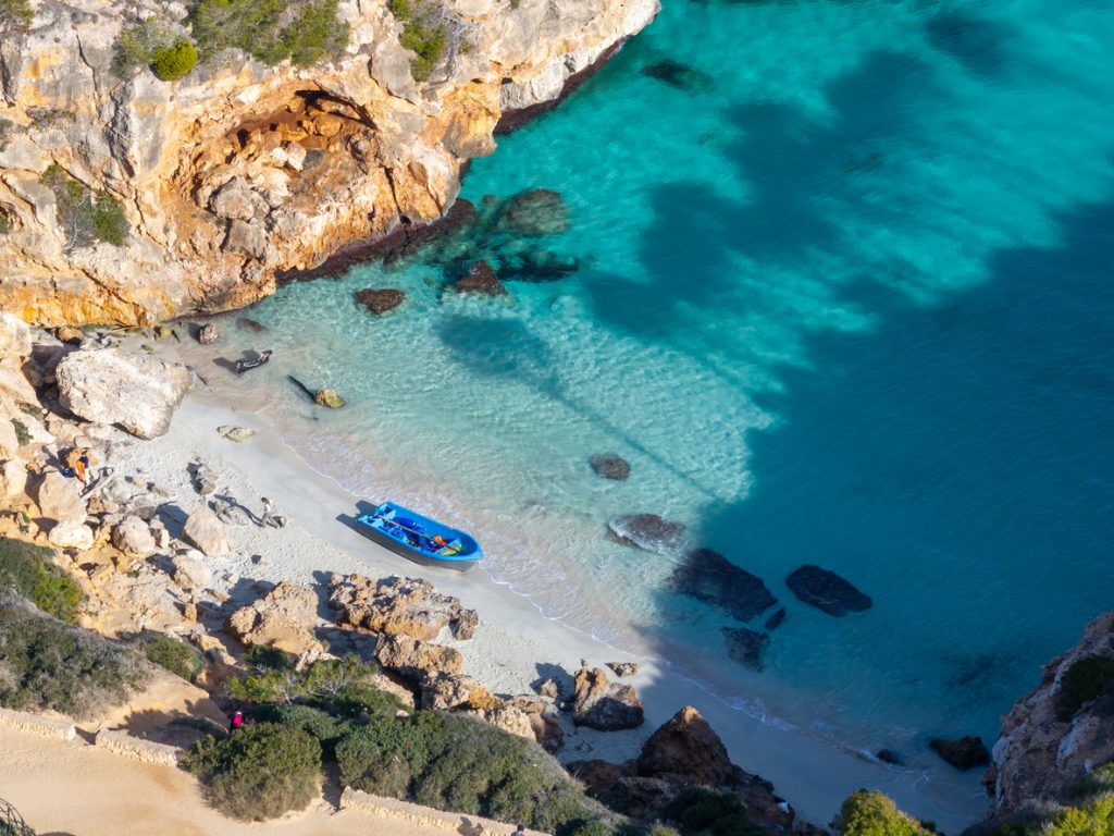 Blick auf die Bucht Caló des Moro mit klarem türkisfarbenem Wasser, Sandstrand und einem Boot am Ufer