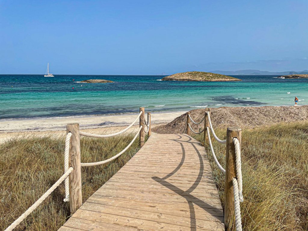 Holzsteg mit Seilen führt durch Dünen zum weißen Sandstrand und türkisblauen Wasser der Playa de Ses Illetes auf Formentera.