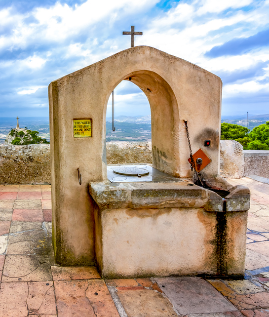 Alter Steinbrunnen mit Kreuz am Kloster Sant Salvador bei Felanitx auf Mallorca mit Blick auf das Tal