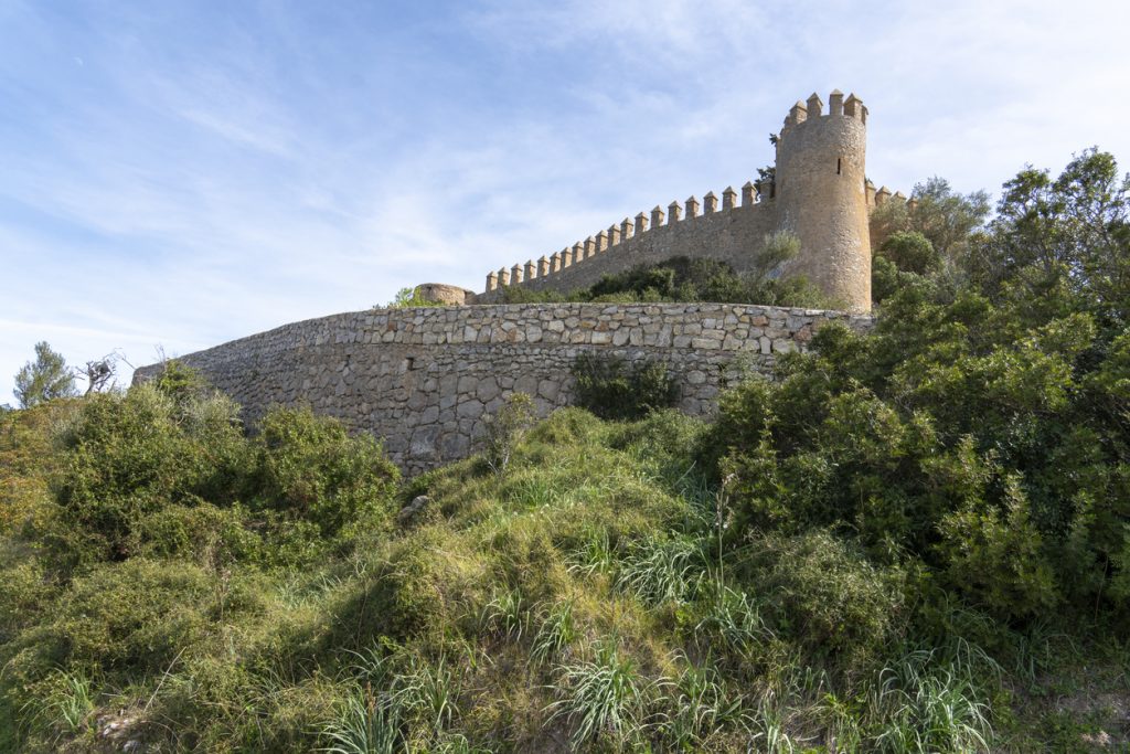 Blick auf eine historische Festungsmauer im Naturpark Llevant auf Mallorca, umgeben von grüner Vegetation unter blauem Himmel.