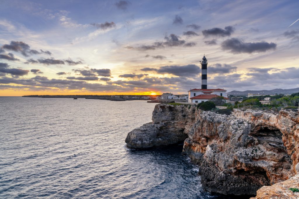 Leuchtturm von Portocolom auf einer Klippe an der Küste Mallorcas bei Sonnenuntergang.