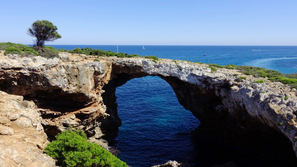 Natürlicher Felsbogen an der Küste der Cala Varques auf Mallorca mit Blick auf das tiefblaue Meer.