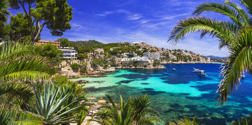 Blick auf Cala Fornells mit kristallklarem Wasser, Booten, Ferienhäusern an der Steilküste und üppiger Vegetation