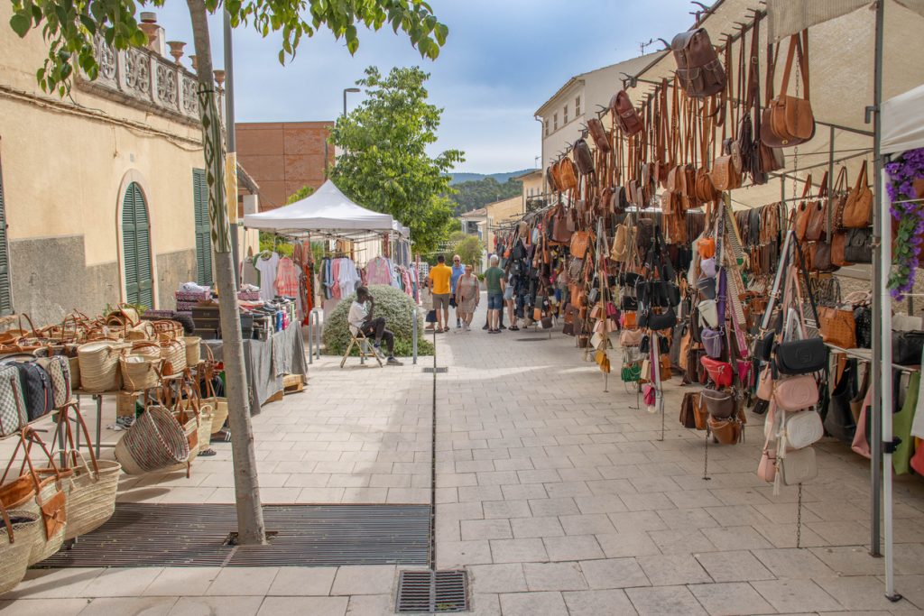 Marktstände auf dem Wochenmarkt in Son Servera auf Mallorca mit Lederwaren, Taschen, Kleidung und handgefertigten Korbwaren, Besucher schlendern durch die Gasse.