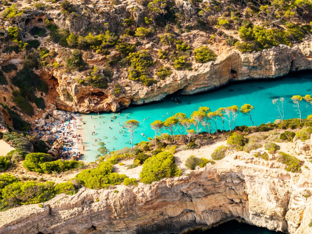 Luftaufnahme der Caló des Moro mit zahlreichen Badenden im türkisfarbenen Wasser und am kleinen Sandstrand