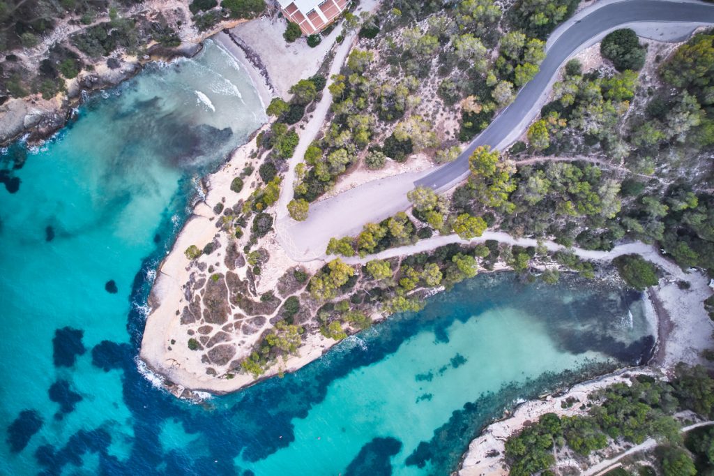 Luftbild der Cala Mondragó mit türkisblauem Wasser, Sandstrand und umliegenden Pinienwäldern im Naturpark Mondragó auf Mallorca.