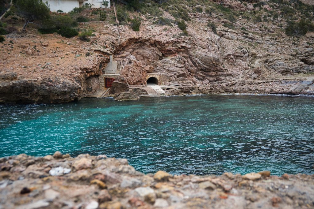 Felsige Küste in Cala Sant Vicenç mit traditionellem Bootshaus direkt am türkisfarbenen Meer