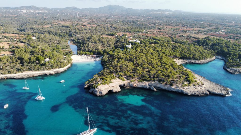 Luftaufnahme der Cala Mondragó mit weißen Sandstränden, türkisblauem Wasser und grünen Pinienwäldern auf Mallorca.