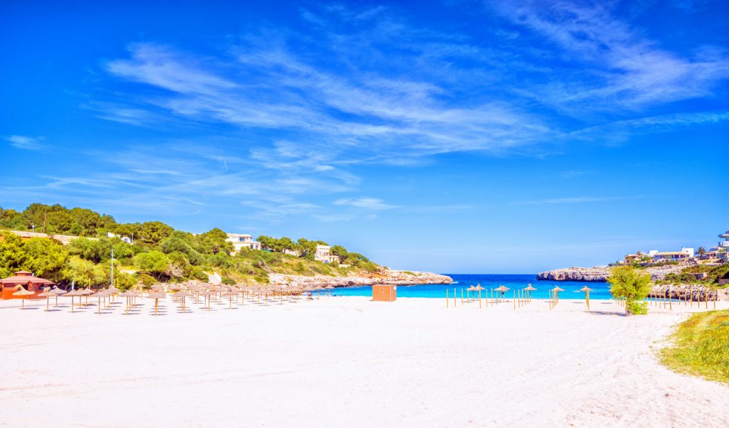 Strand Cala Marçal bei Portocolom auf Mallorca mit hellem Sand, Sonnenschirmen und kristallklarem Meer.