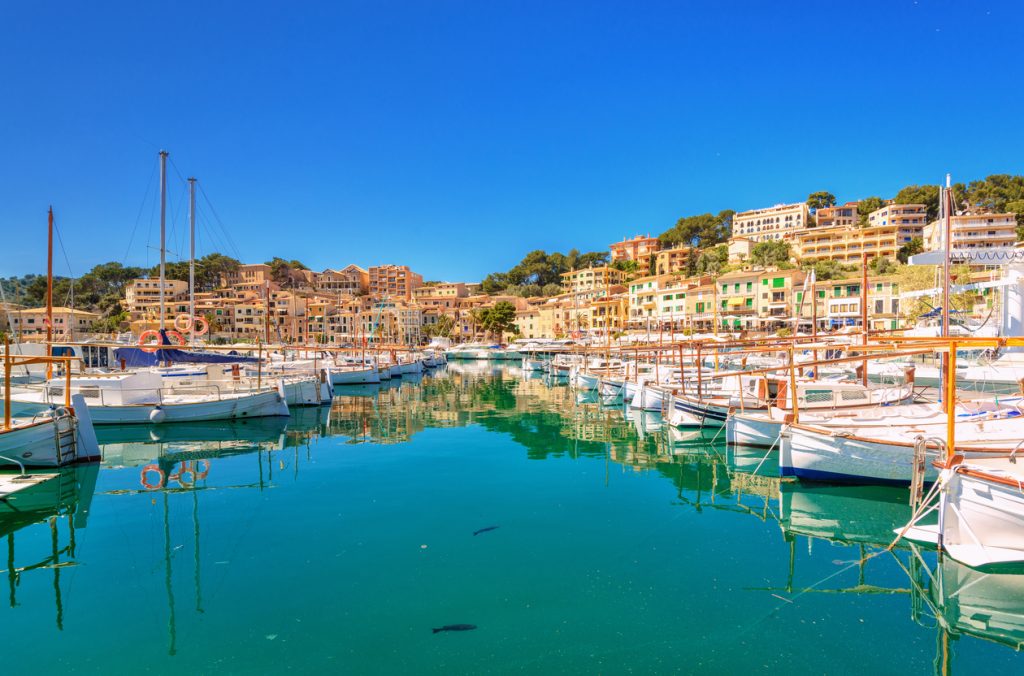 Blick auf die ruhige Hafenbucht von Port de Sóller mit traditionellen Fischerbooten und farbenfrohen Häusern im Hintergrund
