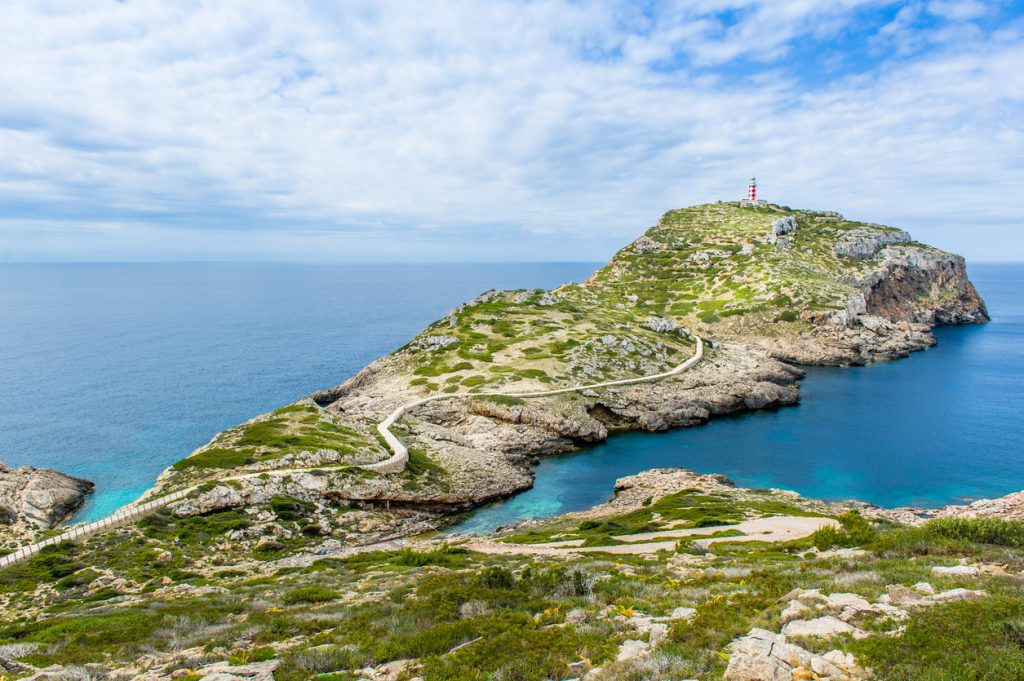 Felsige Halbinsel auf Cabrera mit rot-weißem Leuchtturm, Wanderpfad und Blick auf das offene Meer
