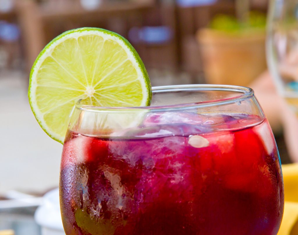 Nahaufnahme eines Glases mit roter Sangria, Eiswürfeln und einer frischen Limettenscheibe am Glasrand.