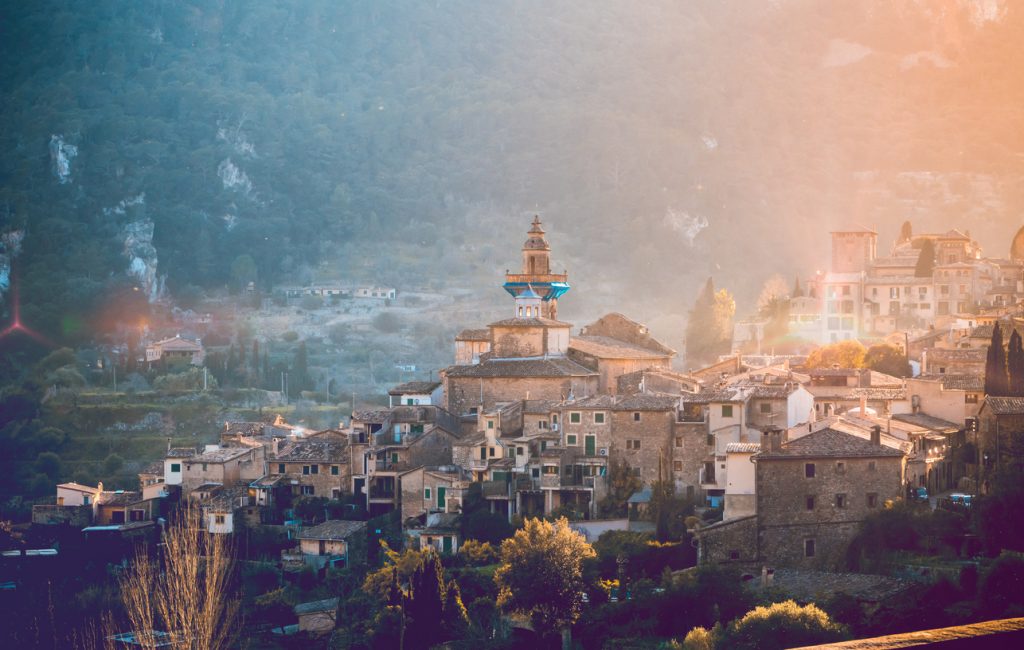 Blick auf das malerische Bergdorf Valldemossa auf Mallorca im warmen Abendlicht, mit dem markanten Turm des Kartäuserklosters vor den Bergen der Serra de Tramuntana.