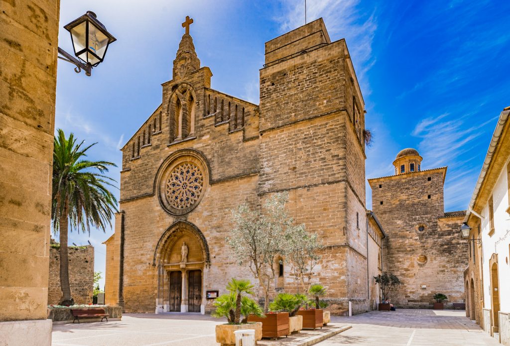Historische Kirche Sant Jaume in der Altstadt von Alcudia auf Mallorca mit Rosettenfenster und Platz im Vordergrund.