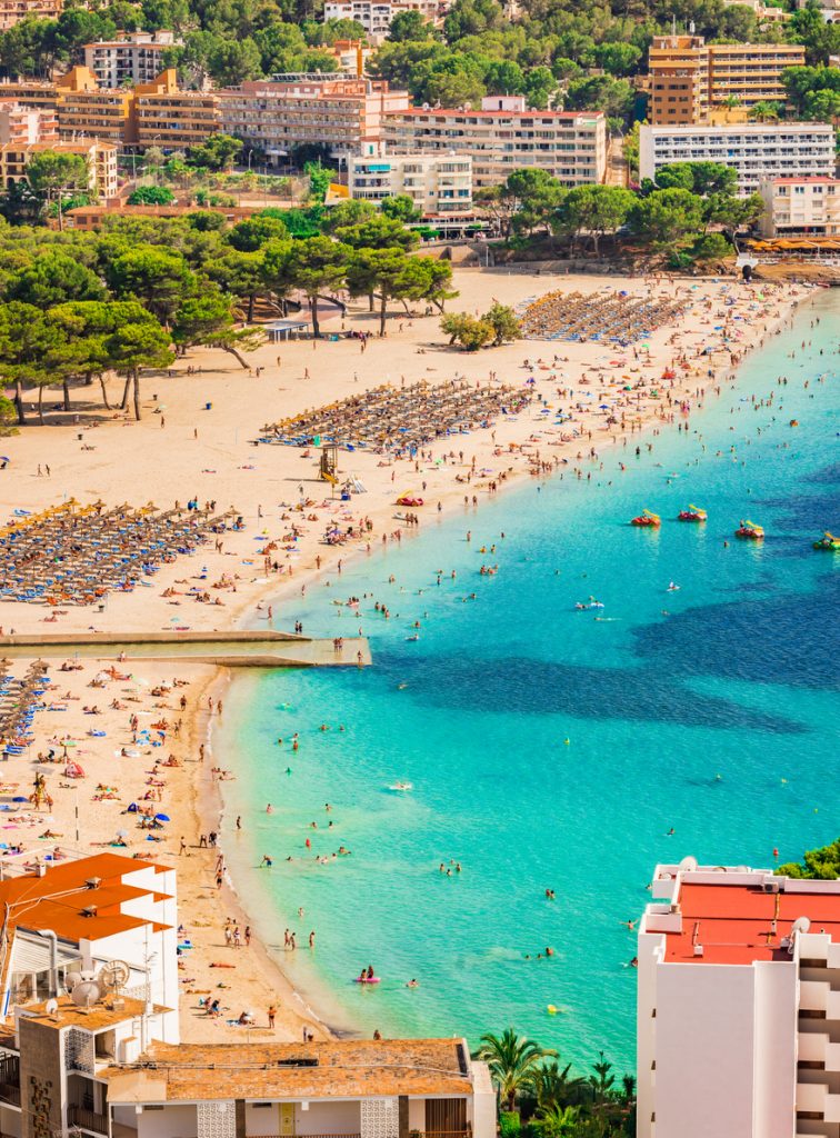 Blick von oben auf den Strand von Santa Ponsa auf Mallorca mit türkisblauem Wasser, Liegestühlen, Sonnenschirmen und zahlreichen Badegästen.