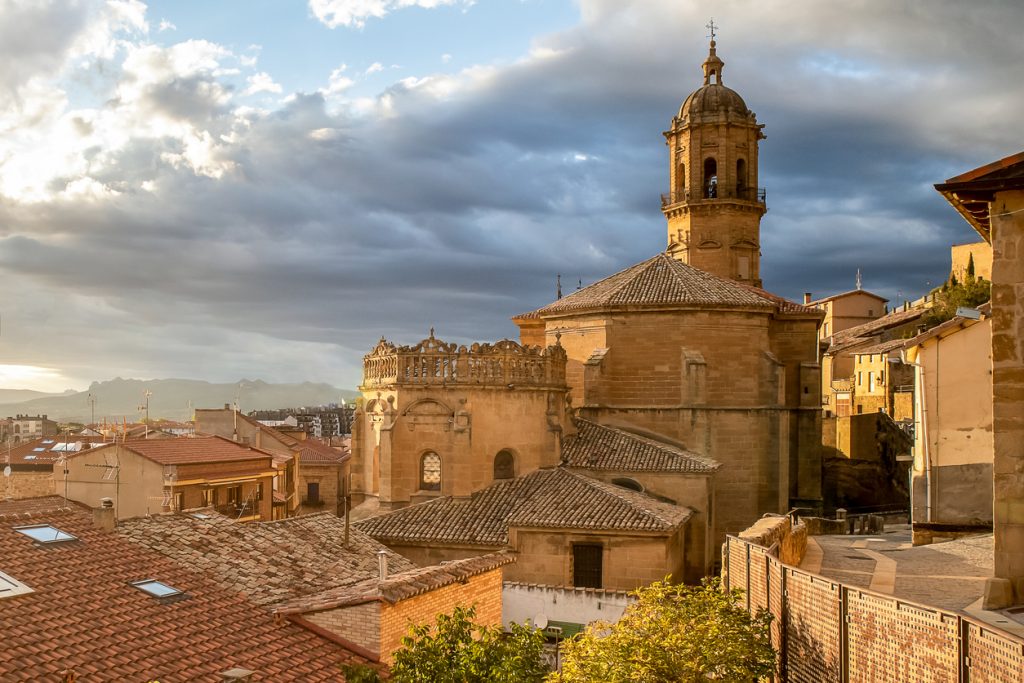 Blick auf die Dächer und eine historische Kirche in Rioja Alavesa bei Sonnenuntergang mit dramatischem Himmel im Hintergrund.