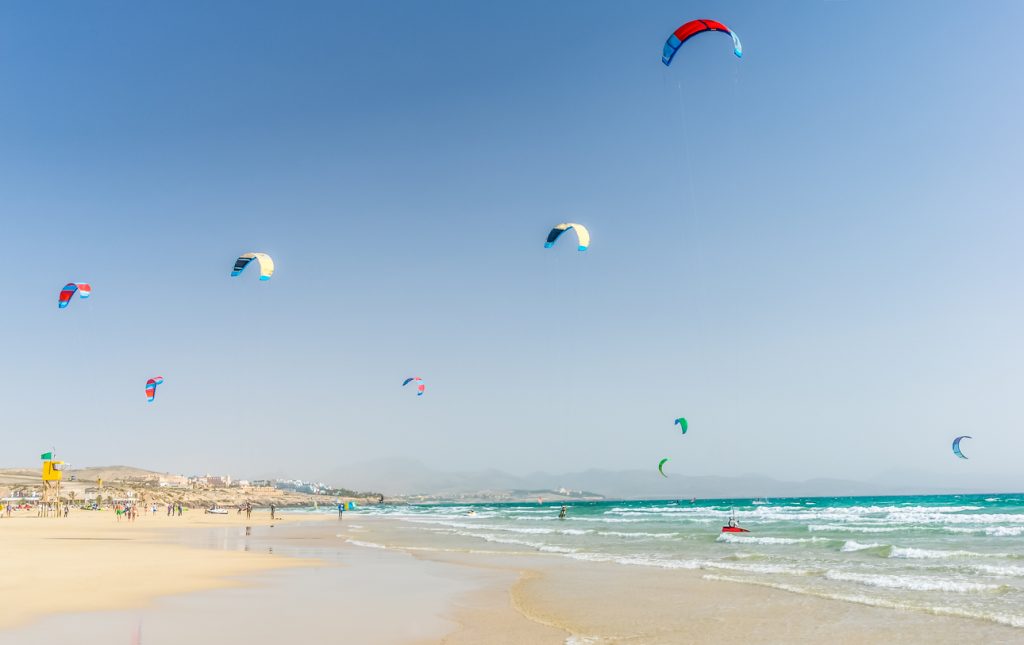 Kitesurfer am Playa de Sotavento auf Fuerteventura mit bunten Segeln über dem türkisblauen Atlantik.